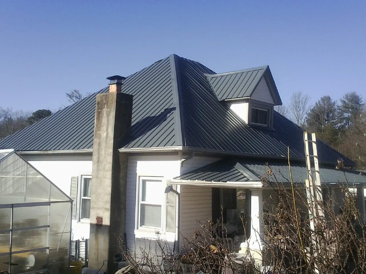 Dark blue standing seam metal roof on a white farmhouse with dormer — Slate & Tile Roof Repair by Roofing Brothers in West Henrietta