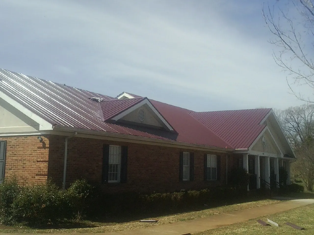 Red metal roof with gabled entries on a long brick building, from a Hail Damage Roof Repair job in West Henrietta