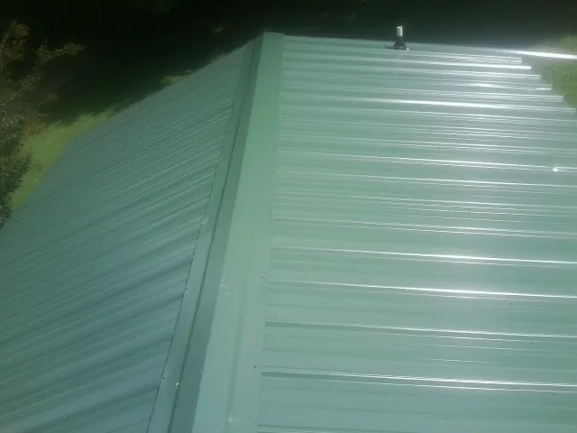 New green metal panels meeting at the ridge of a roof — Flat Roof Repair work by our crew in West Henrietta