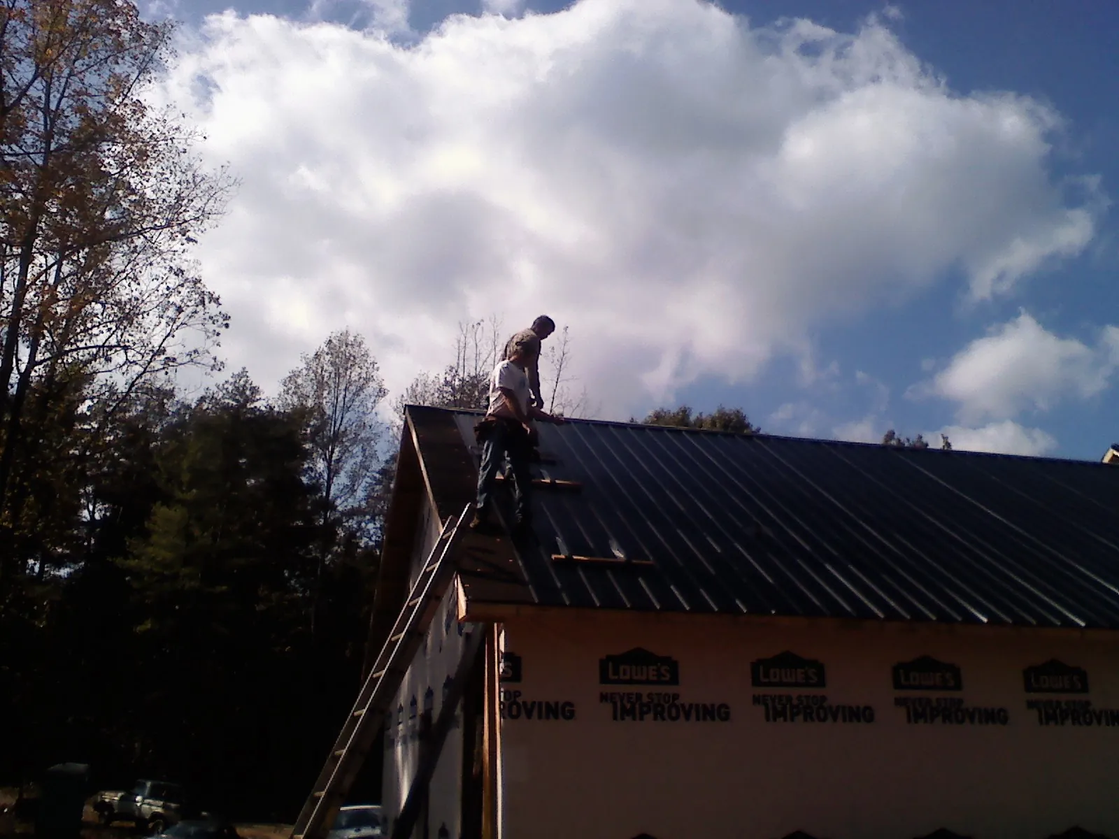 Roofer fastening dark metal panels high against a cloudy sky, from a Roof Inspection job in West Henrietta