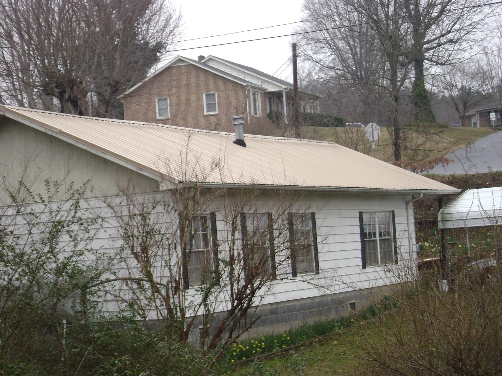 Tan metal roof on a white sided house set into a hillside — Commercial Roofing by Roofing Brothers in West Henrietta