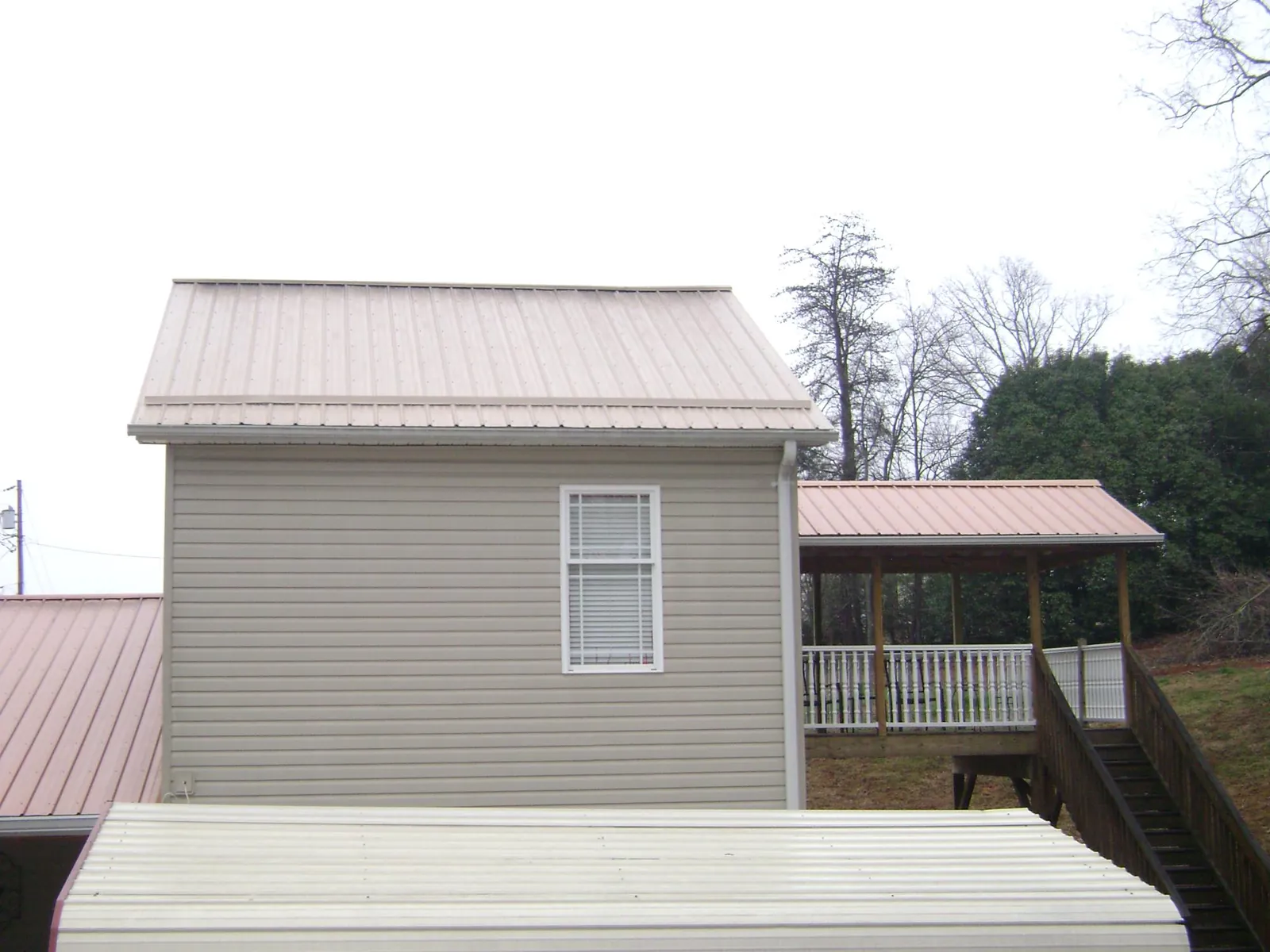 Tan metal roofs on a two story addition and attached porch, from a Roof Replacement job in West Henrietta